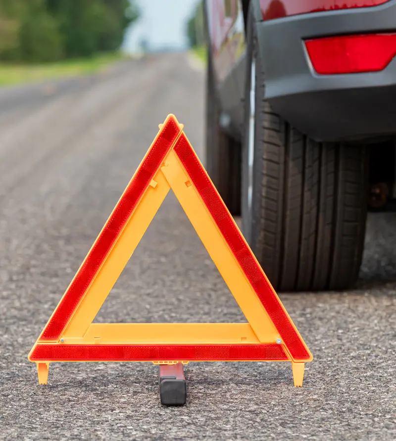 Car breakdown on side of road with warning triangle.