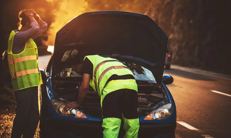 Roadside-mechanic A mobile mechanic looking at a womens car under the hood along the side of the interstate